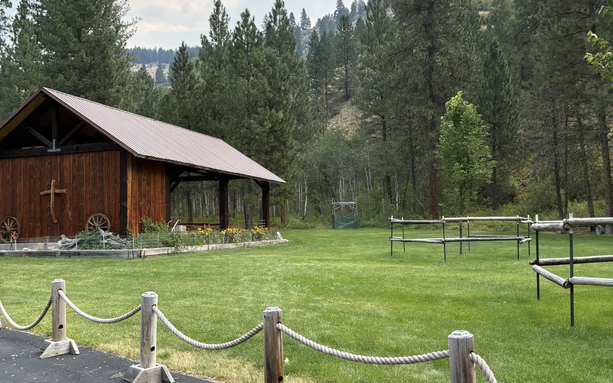 The pavilion's cross-topped end wall with wagon wheels and flower beds, seen across the ceremony lawn.