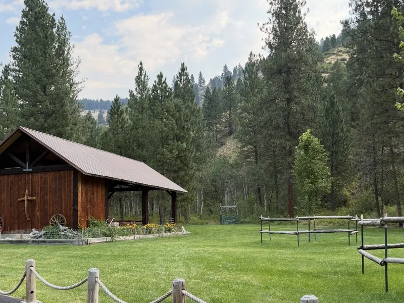 The pavilion's cross-topped end wall and hitching rails on the lawn, with pine-covered mountains rising behind.
