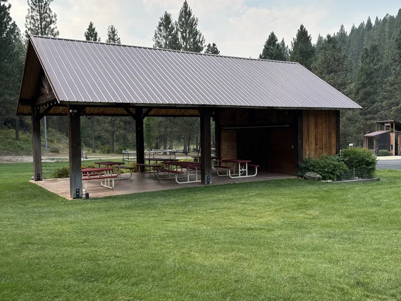 Picnic-table seating under the long covered event pavilion, open on three sides to the lawn.