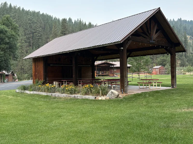 Wildflowers blooming along the base of the pavilion's open corner, with the lawn in front.